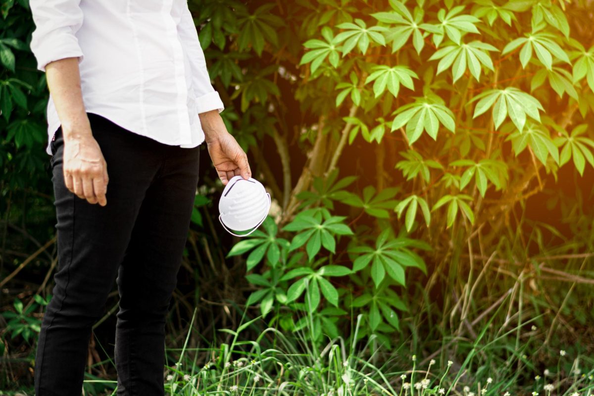 A person standing near lush green plants while holding a protective mask, suggesting a focus on sustainable practices and the impact of cannabis fertilizer on plant health.