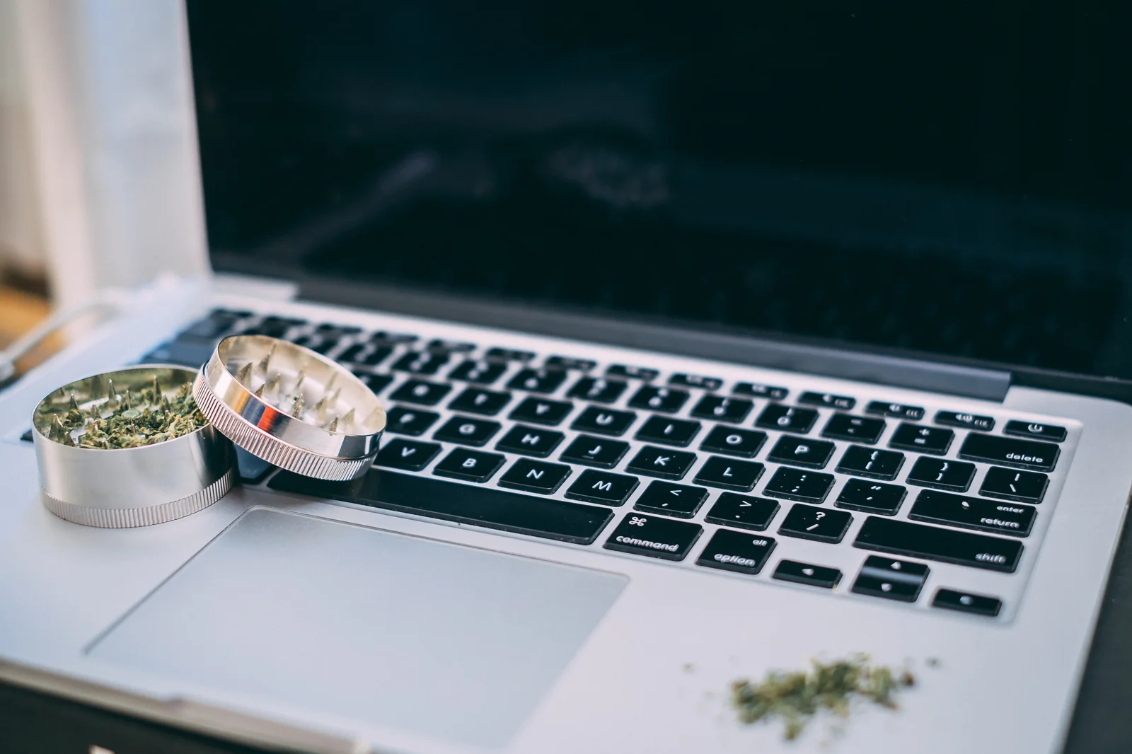 A metal grinder filled with dried cannabis sits on top of a laptop keyboard, with small cannabis pieces scattered nearby. This image symbolizes the integration of cannabis CRM software in managing product inventory and tracking cannabis processing workflows digitally.