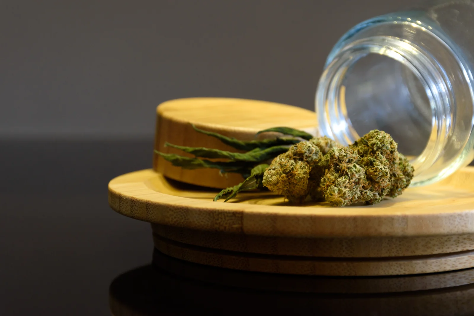 Cannabis buds and dried leaves displayed on a wooden tray with a glass jar, representing product tracking with cannabis seed to sale software.