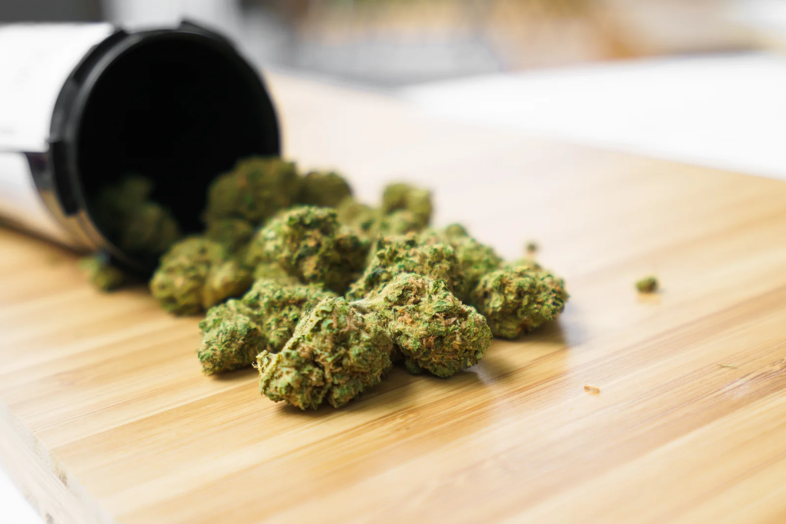 Cannabis buds spilled from a container onto a wooden surface, illustrating retail and inventory tracking using cannabis seed to sale software.