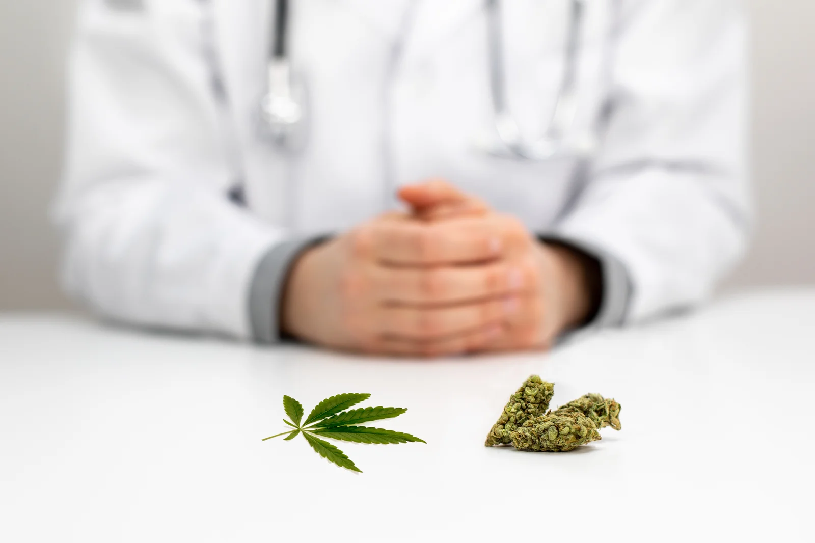 A medical professional in a white coat sits behind a table with a cannabis leaf and buds, showcasing healthy cannabis blooming for medicinal use.