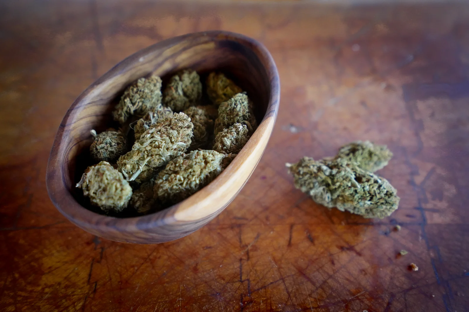 Close-up of dried cannabis buds in a carved wooden bowl on a rustic table, representing product cataloging features of a cannabis software company.