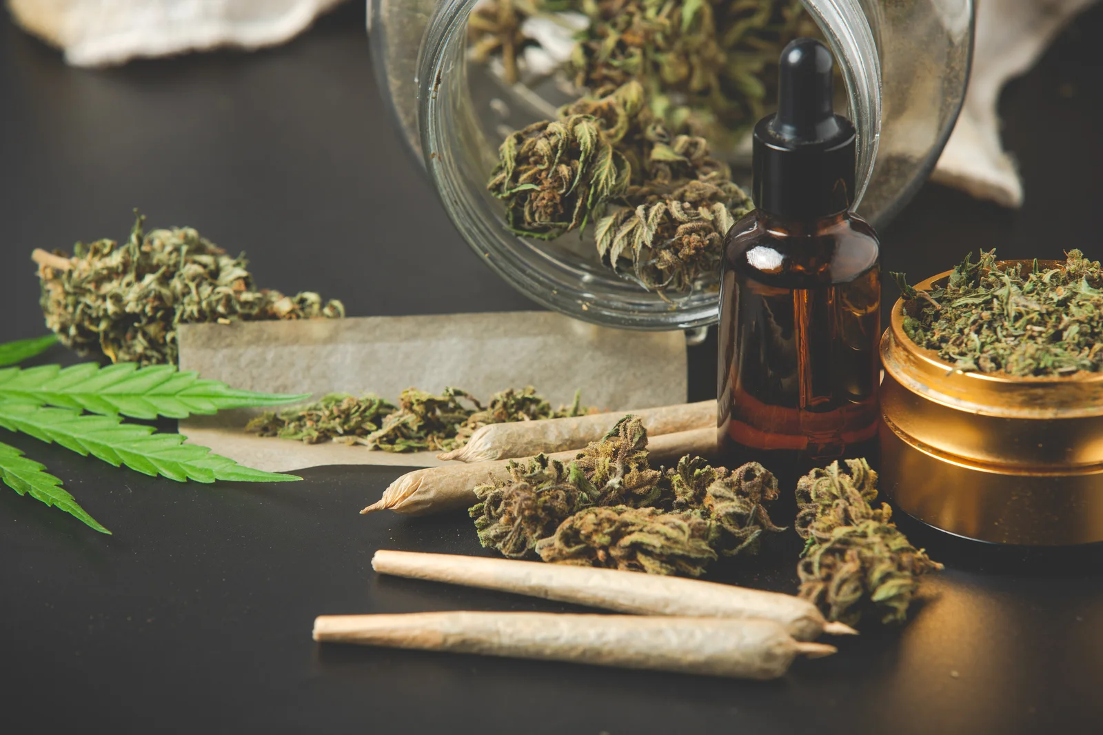 Michigan Cannabis Consultants showcase a selection of cannabis products including pre-rolled joints, dried cannabis buds, oil tincture, and a grinder, arranged on a dark surface for professional presentation.