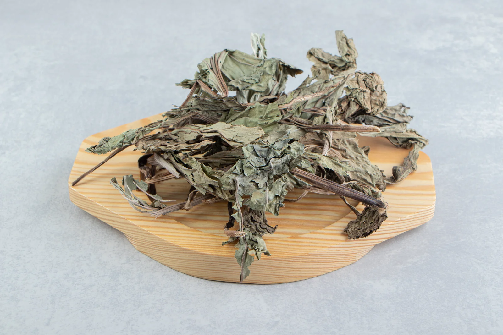 A pile of brittle, dry cannabis leaves and stems placed on a small wooden tray, showing signs of complete dehydration and curing.