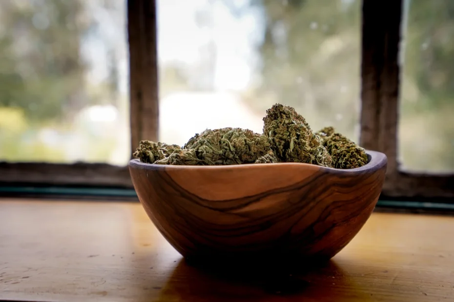 Wooden bowl filled with cured cannabis buds placed on a windowsill in natural light.
