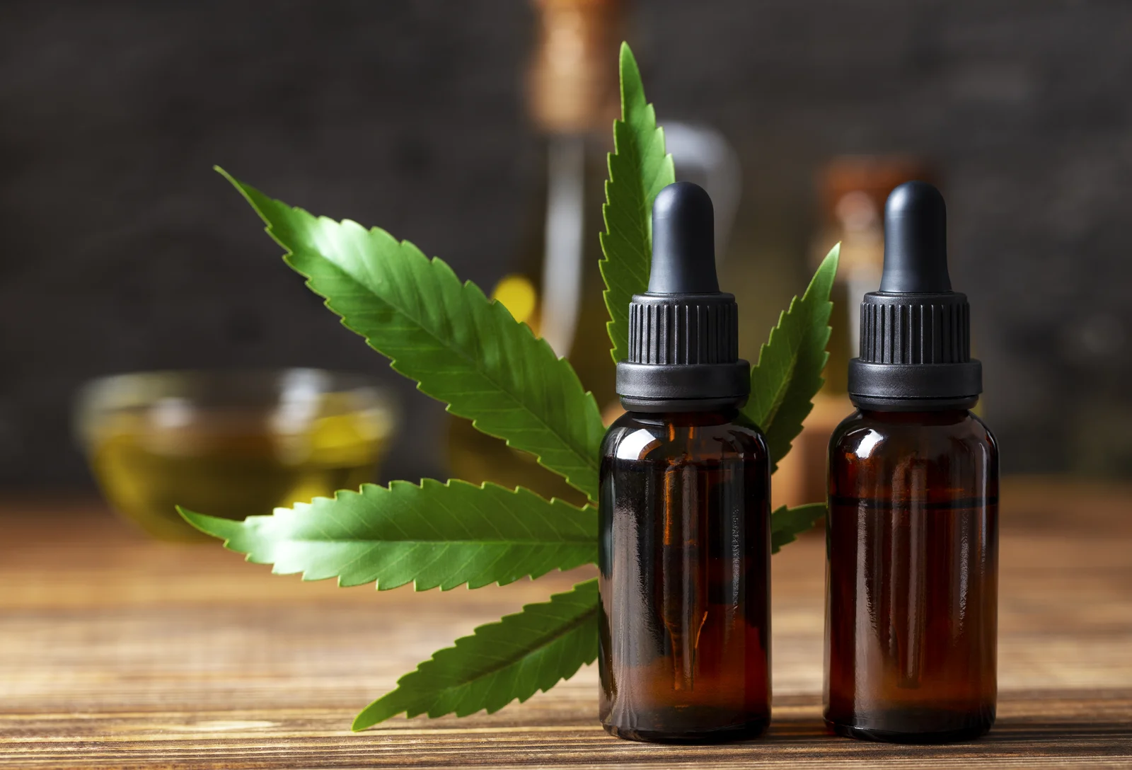 Brown glass dropper bottles with cannabis leaf on wooden table, representing Hemp-Derived CBD wellness products.